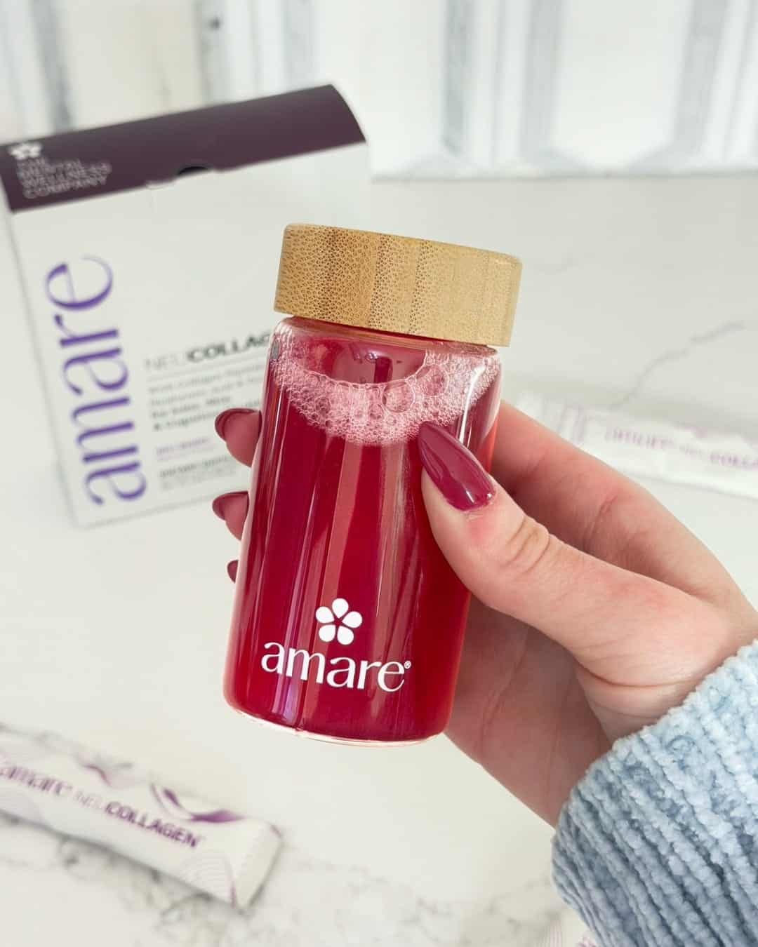 A hand holding a glass of ruby-red NeuCollagen with the box and sachets